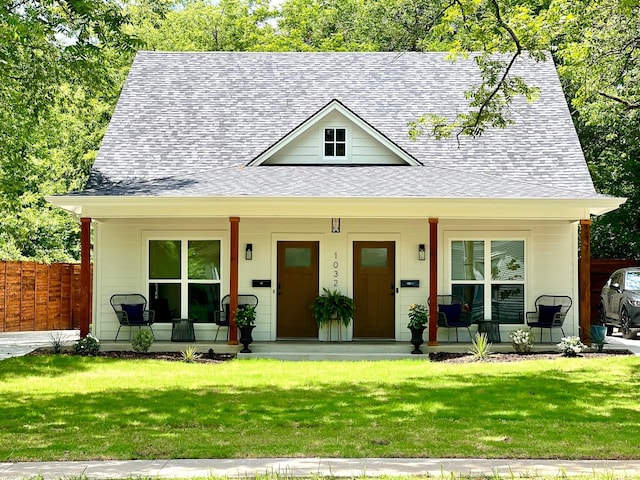 view of front of house with a shingled roof, covered porch, fence, and a front lawn