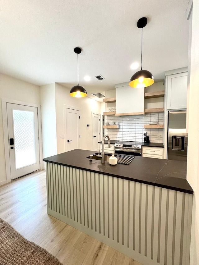 kitchen featuring appliances with stainless steel finishes, backsplash, open shelves, light wood finished floors, and dark countertops