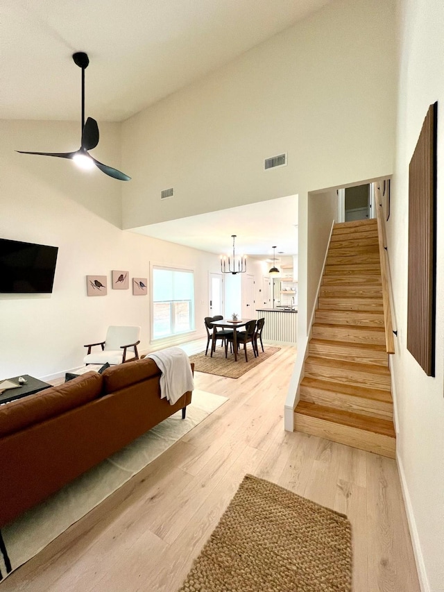 living area featuring ceiling fan with notable chandelier, light wood-style flooring, stairway, and visible vents