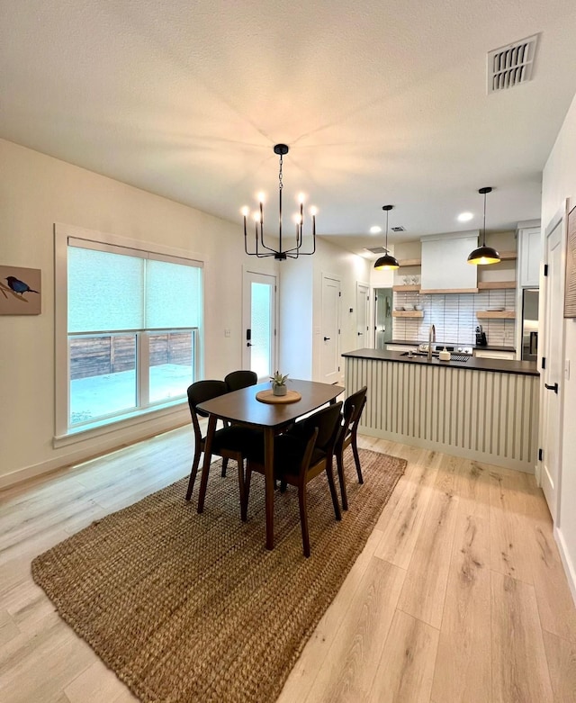 dining area featuring a textured ceiling, a notable chandelier, visible vents, baseboards, and light wood finished floors