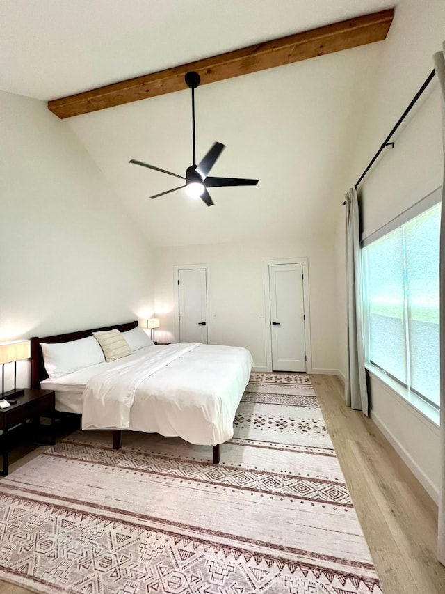 bedroom with baseboards, a ceiling fan, light wood-style flooring, beamed ceiling, and high vaulted ceiling