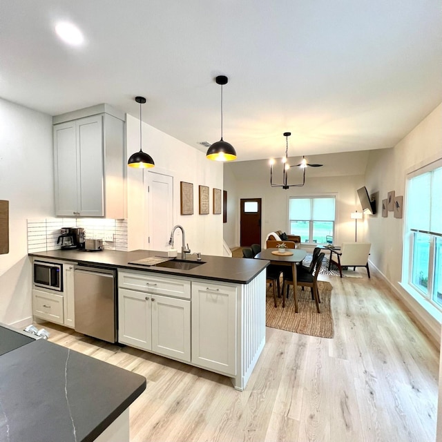 kitchen with dark countertops, light wood-style flooring, appliances with stainless steel finishes, a sink, and a peninsula