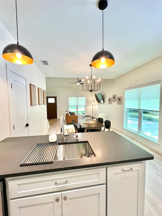 kitchen with a wealth of natural light, dark countertops, pendant lighting, and white cabinetry