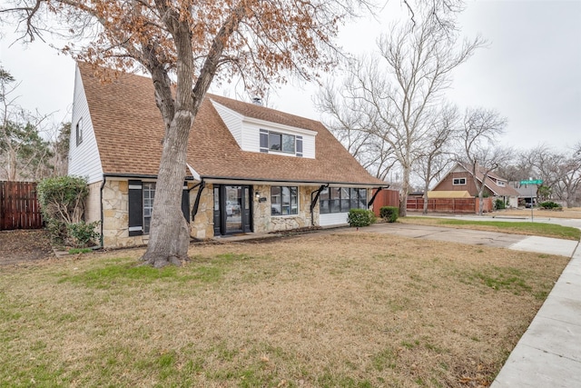 view of front of property with stone siding, fence, a front lawn, and roof with shingles