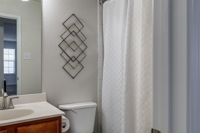 bathroom featuring a shower with shower curtain, a textured wall, vanity, and toilet