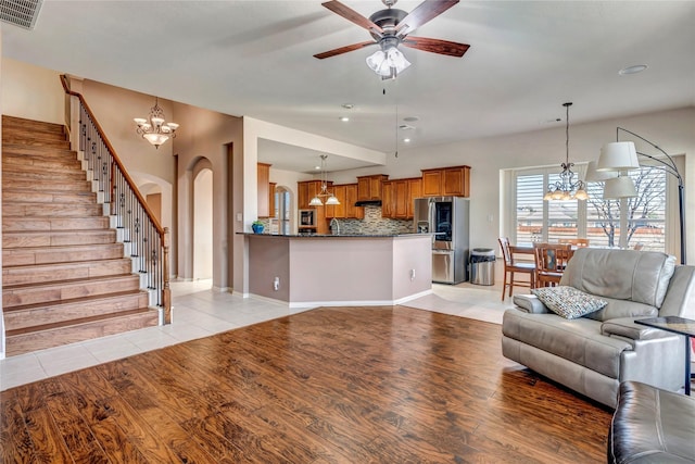 unfurnished living room with arched walkways, light wood finished floors, visible vents, stairway, and ceiling fan with notable chandelier