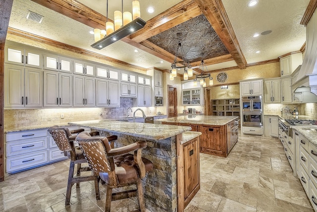 kitchen featuring stone tile floors, an island with sink, a breakfast bar, beamed ceiling, and backsplash