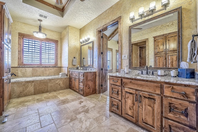 bathroom with visible vents, a sink, a textured ceiling, and a garden tub