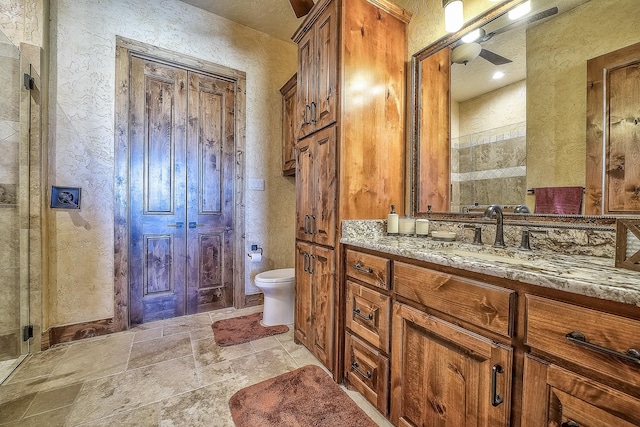 bathroom featuring vanity, a tile shower, toilet, and stone tile floors