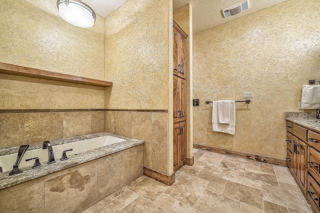 bathroom featuring visible vents, stone finish flooring, a textured ceiling, vanity, and a bath