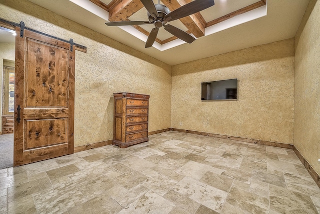 spare room featuring stone finish flooring, a barn door, a ceiling fan, and baseboards