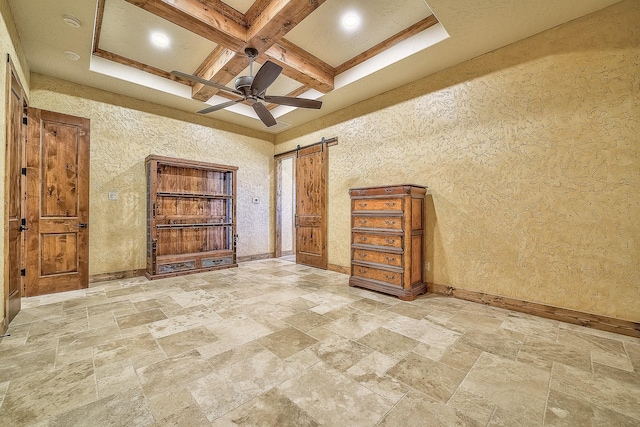 unfurnished bedroom with beam ceiling, a barn door, stone finish flooring, coffered ceiling, and baseboards