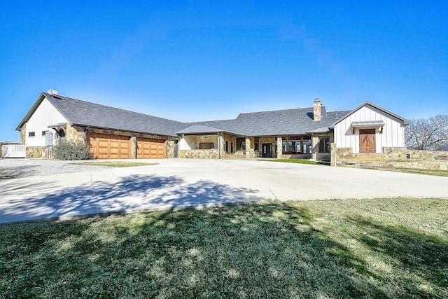 modern farmhouse style home with driveway, stone siding, a chimney, a front lawn, and board and batten siding