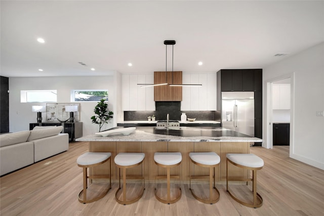 kitchen with a large island, a breakfast bar area, tasteful backsplash, modern cabinets, and built in refrigerator