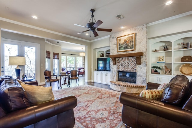 living area with ceiling fan, built in shelves, a fireplace, visible vents, and crown molding