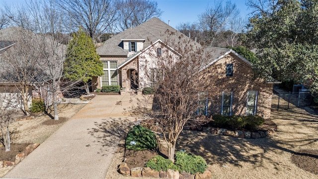 view of front of house with brick siding, a shingled roof, and fence