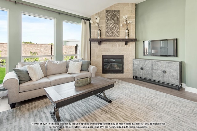 living area with vaulted ceiling, a stone fireplace, baseboards, and wood finished floors