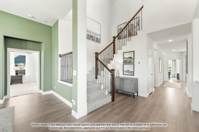 stairs featuring a high ceiling, baseboards, wood finished floors, and recessed lighting