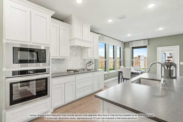 kitchen with visible vents, white cabinets, decorative backsplash, stainless steel appliances, and a sink