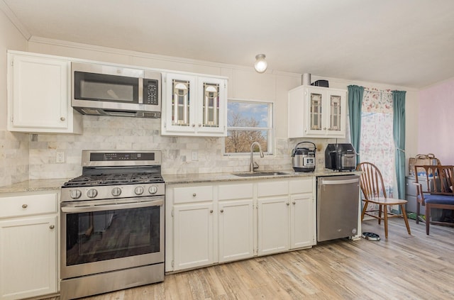 kitchen featuring decorative backsplash, appliances with stainless steel finishes, light stone countertops, light wood-style floors, and a sink