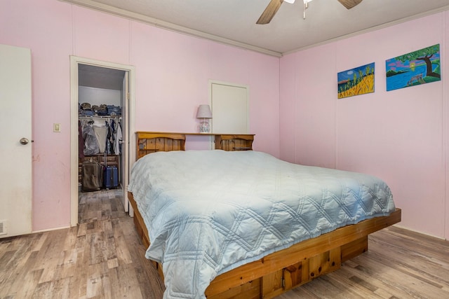 bedroom featuring ornamental molding, a closet, wood finished floors, and a walk in closet