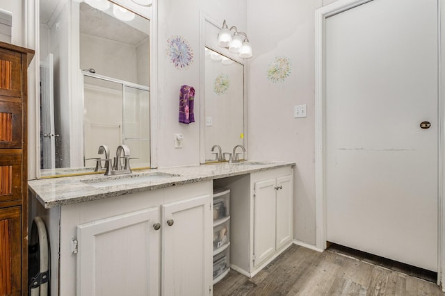 full bath with double vanity, wood finished floors, a sink, and a shower with door