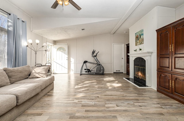 living area featuring lofted ceiling, ceiling fan, a fireplace, and light wood-style flooring