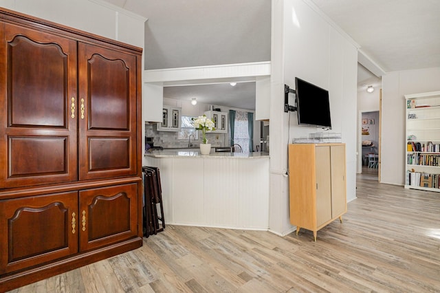 kitchen with light wood-style flooring, decorative backsplash, vaulted ceiling, and a sink