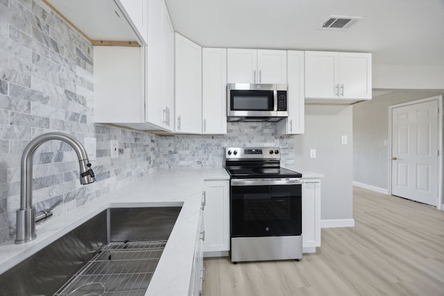 kitchen with light countertops, decorative backsplash, appliances with stainless steel finishes, white cabinets, and a sink