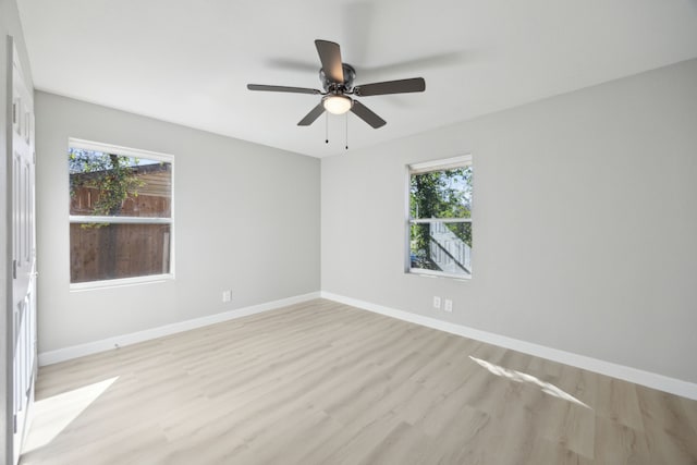 empty room with light wood finished floors, a wealth of natural light, and baseboards