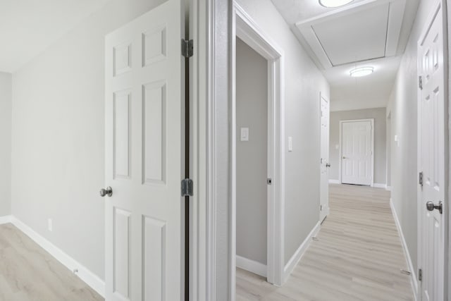 hall featuring attic access, light wood-style flooring, and baseboards