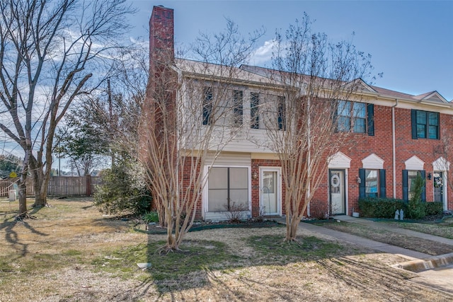 view of front of house featuring brick siding, a chimney, and fence