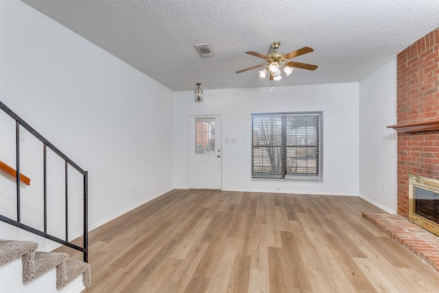 unfurnished living room featuring visible vents, a ceiling fan, light wood-style flooring, stairway, and a fireplace