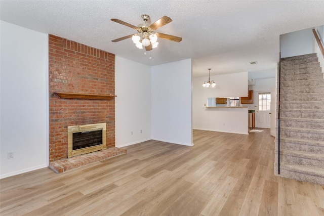 unfurnished living room with a brick fireplace, light wood-style flooring, stairs, and a textured ceiling