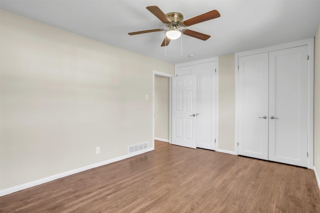 unfurnished bedroom with baseboards, visible vents, ceiling fan, wood finished floors, and a closet