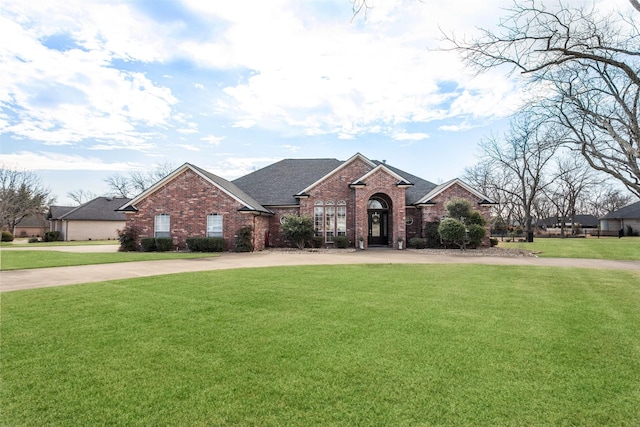 view of front of property with a shingled roof, brick siding, driveway, and a front lawn