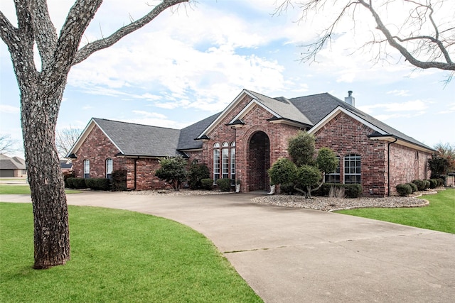 view of front of house featuring brick siding, roof with shingles, a chimney, concrete driveway, and a front lawn