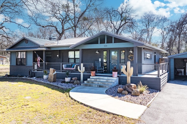 view of front facade with a front yard, covered porch, metal roof, and an outbuilding