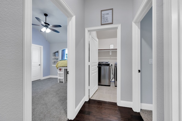 hallway with washer and clothes dryer, dark colored carpet, dark wood-type flooring, vaulted ceiling, and baseboards