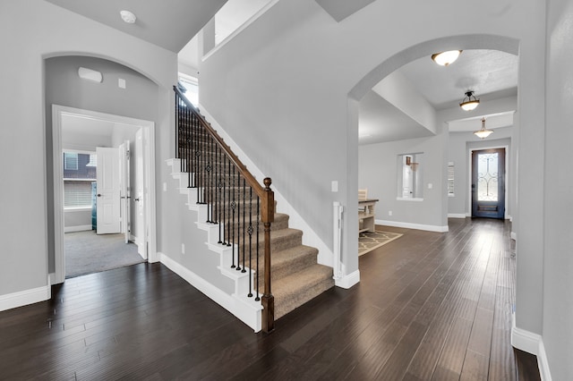 foyer featuring arched walkways, dark wood finished floors, stairs, and baseboards