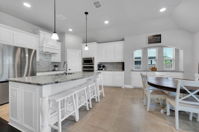 kitchen with stainless steel appliances, visible vents, custom range hood, white cabinetry, and light stone countertops