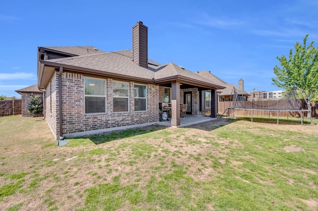 back of property featuring a lawn, a patio, a fenced backyard, a chimney, and a trampoline