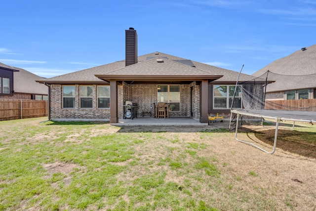 rear view of property with a trampoline, roof with shingles, a chimney, a patio area, and fence