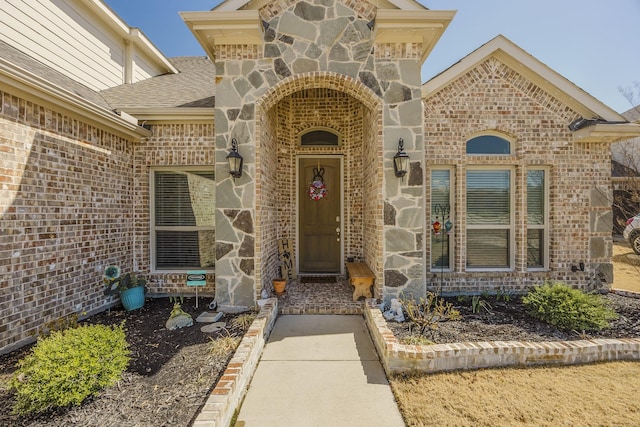 entrance to property with stone siding, roof with shingles, and brick siding