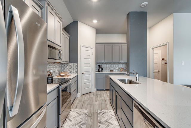 kitchen featuring appliances with stainless steel finishes, gray cabinets, a sink, and decorative backsplash