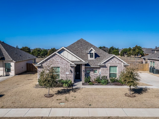 craftsman-style home featuring central AC, brick siding, a shingled roof, fence, and board and batten siding