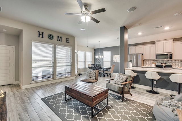 living area featuring ceiling fan with notable chandelier, light wood finished floors, visible vents, and baseboards