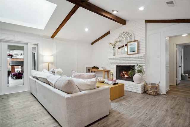 living area with vaulted ceiling with beams, light wood-style floors, a fireplace, and a decorative wall