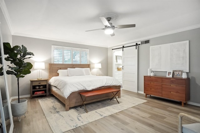 bedroom with a barn door, visible vents, baseboards, light wood-style floors, and ornamental molding