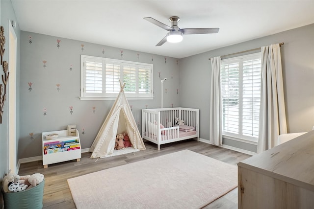 bedroom with a nursery area, multiple windows, wood finished floors, and baseboards